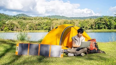 Young man camping and charging laptop with using portable solar panel