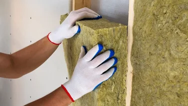 Installer with white and blue gloves on puts a panel of rock wool insulation into the wall