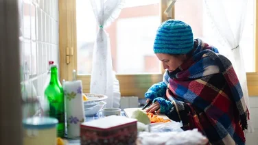 woman wrapped up in blanket and wool hat cutting carrots in kitchen