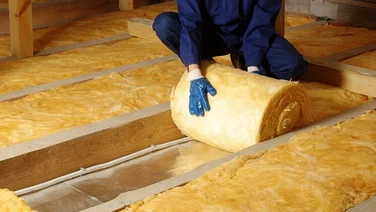 An installer dressed in navy overalls rolls out yellow fibre floor insulation