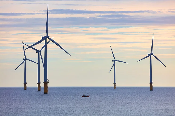 Offshore windfarm, UK, North Yorkshire. A tiny fishing boat is dwarfed by the scale of the wind turbines.
