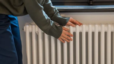 Woman warming hands on white radiator at home