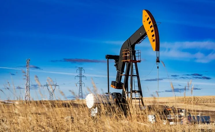 A black and yellow fracking machine with clear blue skies in the background and dried grass in the foreground