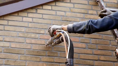 Someone Installing cavity wall insulation into the wall through a small hole