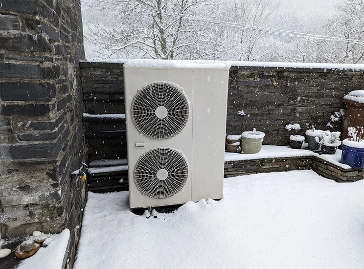 outdoor unit of heat pump against stone wall in snowy garden